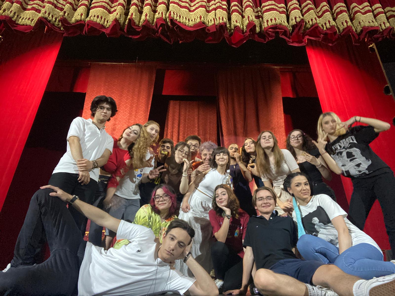 Victor with a theatre group on a stage framed by red curtains.